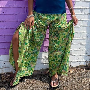 Puede incluir: Pantalones anchos con una base de color verde vibrante y un intrincado estampado floral y de cachemira en tonos amarillo, rosa y verde oscuro. Los pantalones tienen aberturas laterales altas en cada pierna, un corte holgado y se combinan con una camiseta sin mangas de color verde azulado.