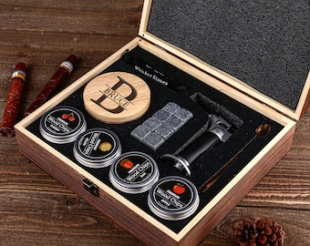 Peut inclure: Coffret cadeau en bois avec accessoires pour whisky. Il comprend un dessous de verre en bois avec "BRUCE", des pierres à whisky, un briquet torche, une cuillère et des boîtes de copeaux de bois. Deux cigares sont visibles.