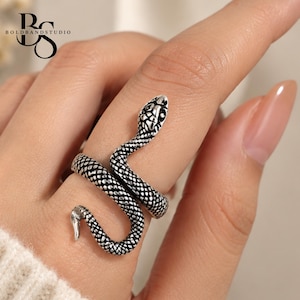 May include: A silver-toned metal ring shaped like a coiled snake with textured scales and a detailed head. The ring wraps around the finger, featuring an oxidised finish that highlights the intricate pattern of the serpent's body and scales.