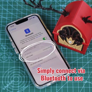Może przedstawiać: Smartfon wyświetla ustawienia Bluetooth, połączony z "DAU Audio". Czerwony głośnik dekoracyjny ze złotymi akcentami znajduje się w pobliżu. Widoczny jest tekst "Simply connect via Bluetooth to use".