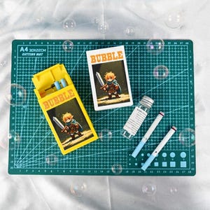 May include: A yellow rectangular box labeled BUBBLE featuring a pixel art character holding a sword, a matching white box, a small clear glass vial with a white label, and two thin white and light blue wands for blowing bubbles.