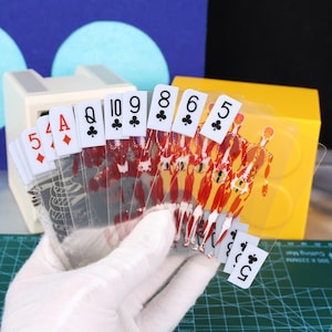 May include: A deck of clear playing cards with a unique anatomical design. The cards feature red and white illustrations of the human body, with traditional suit symbols and card values. The cards are held in a gloved hand.