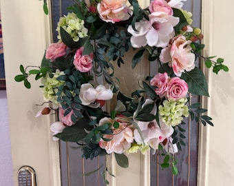 Preciosa corona de magnolias y rosas sobre una base de vid. No necesita lazo. Se sostiene sola.