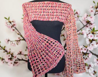Puede incluir: Un bolero de ganchillo rosa, naranja y crema con mangas acampanadas. El diseño de tejido abierto se muestra en un maniquí negro. El top sin hombros es un accesorio de moda único.