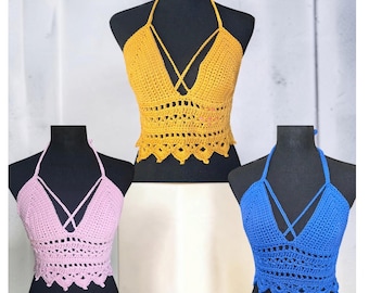 May include: Three crochet halter tops in yellow, light pink, and blue. Each top features a deep V-neckline with crisscross straps, a textured midsection, and a scalloped hemline. The garments are displayed on black mannequins.
