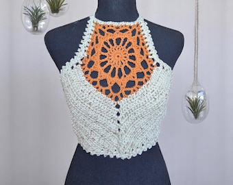 Puede incluir: Top halter de ganchillo hecho a mano en hilo verde claro moteado con un diseño central naranja. El top presenta un patrón calado detallado y un diseño de cuello halter. La prenda se exhibe en un maniquí negro.