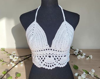 Puede incluir: Top halter de ganchillo blanco hecho a mano, exhibido en un maniquí negro. El top presenta un diseño de cuello en V y un patrón calado decorativo en la parte inferior. Hecho de hilo blanco, es un artículo de moda de verano.