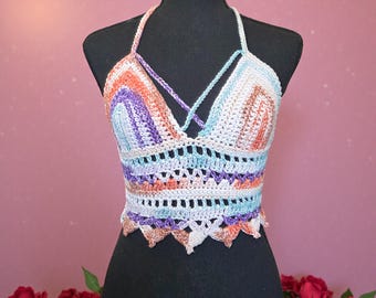 Puede incluir: Top halter de ganchillo hecho a mano en colores del arcoíris, incluyendo naranja, morado y azul. El top presenta un diseño entrecruzado en el busto y un borde festoneado. La prenda se exhibe en un maniquí negro.