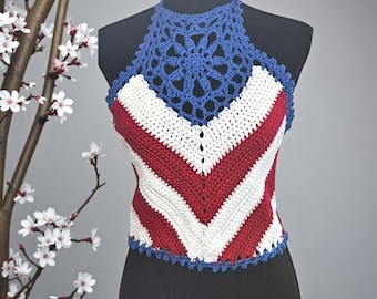 Puede incluir: Top halter de ganchillo hecho a mano en rojo, blanco y azul. El top presenta un patrón de chevron en rojo y blanco, con un cuello halter azul y un diseño floral decorativo. Los dobladillos están ribeteados en azul.