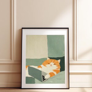 May include: A framed art print showing a ginger and white cat using a laptop. The cat is lying down on a green and cream-coloured background. The artwork is in a black frame and is leaning against a wall.
