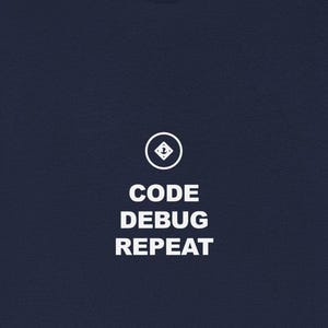 May include: Navy blue t-shirt with the text "CODE DEBUG REPEAT" in white, centered on the front. Above the text is a white graphic of a downward-pointing arrow inside a circle. The shirt is made of a soft material.