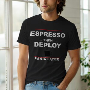 Può includere: T-shirt nero con la scritta bianca e rossa "ESPRESSO - THEN - DEPLOY - PANIC LATER". La maglietta presenta una grafica di una tazza di caffè. La maglietta è indossata da una persona.