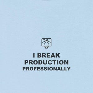 May include: Light blue t-shirt with the text "I BREAK PRODUCTION PROFESSIONALLY" in black. The shirt has a simple graphic above the text. The t-shirt is made of a soft material.