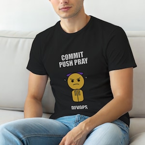 May include: Black t-shirt with the text "COMMIT PUSH PRAY" above a yellow emoji with a purple halo and an angry face. The word "DEVNPS" is printed below the emoji.