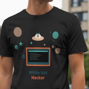 May include: Black t-shirt with a graphic featuring a computer screen, planets, and a UFO. The text "White Hat Hacker" is printed below the graphic in white and orange. The shirt is made of a soft material.