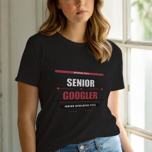 Op de afbeelding: Zwart t-shirt met de tekst "SENIOR GOOGLER" in wit en rood. Het shirt bevat ook de tekst "OFFICIAL TITLE" en "JUNIOR DEVELOPER TITLE".