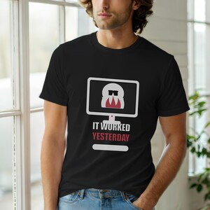 Puede incluir: Camiseta negra con un gráfico de pantalla de ordenador blanca que muestra una cara de dibujos animados con gafas de sol y una corbata roja. El texto "IT WORKED YESTERDAY" está debajo en rojo y blanco.