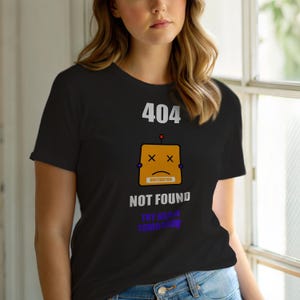 Op de afbeelding: Zwart T-shirt met een afbeelding van een robotgezicht en de tekst "404 NOT FOUND". De robot heeft een oranje hoofd, doorgestreepte ogen en een verdrietige mond. De tekst "TRY AGAIN TOMORROW" staat eronder.