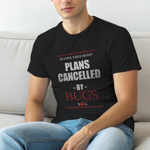 Puede incluir: Camiseta negra con el texto "WEEKEND CODER ENERGY PLANS CANCELLED BY BUGS". El texto es en blanco y rojo, con un pequeño gráfico de error. La camiseta la lleva una persona.