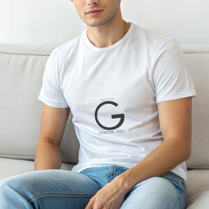 May include: White t-shirt with a black "G" graphic and the text "SENIOR" above and "JUNIOR DEV" below. The shirt is worn with blue jeans.