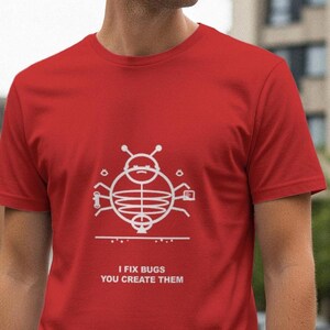 Op de afbeelding: Een rood t-shirt met een witte afbeelding van een insect en de tekst "I FIX BUGS YOU CREATE THEM". Het shirt met korte mouwen is gemaakt van een zacht materiaal.