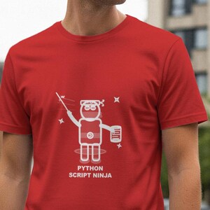 May include: Red t-shirt with a white graphic of a ninja holding a wand and a scroll. The text "PYTHON SCRIPT NINJA" is printed below the graphic. The shirt is short-sleeved and made of a soft material.