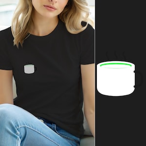Może przedstawiać: Czarny t-shirt z krótkim rękawem z małą grafiką na lewej piersi. Grafika przedstawia biały kubek z czarnym uchem i jaskrawozielonym brzegiem, z trzema małymi czarnymi liniami pary unoszącymi się nad górną częścią kubka.
