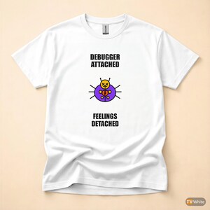 Op de afbeelding: Wit T-shirt met de tekst "DEBUGGER ATTACHED" boven een afbeelding van een paarse, gele en zwarte kever met een gebroken hart, en de tekst "FEELINGS DETACHED" eronder. Het shirt is gemaakt van een zacht materiaal.