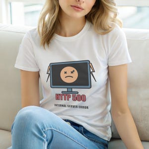 Puede incluir: Camiseta blanca con una pantalla de ordenador de dibujos animados que muestra una cara triste y el texto "HTTP 500 INTERNAL SERVER ERROR" en rojo. La pantalla es negra con una cara naranja claro. La camiseta es de manga corta.