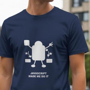May include: Navy blue t-shirt with a white graphic of a robot-like figure and the text "JAVASCRIPT MADE ME DO IT". The design includes stars and rectangular shapes. The shirt is short-sleeved.