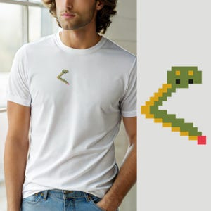 May include: A white short-sleeved t-shirt featuring a small pixel art graphic on the left chest. The graphic depicts a green and yellow snake-like shape with a red square at the tip of its tail, rendered in a blocky, digital aesthetic.