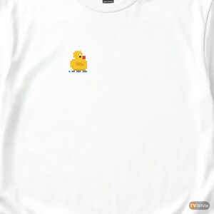 Op de afbeelding: Wit shirt met lange mouwen met een gepixeld geel eendenontwerp, rode snavel en blauwe waterlijnen. De eendenafbeelding staat op de borst. Het shirt is gemaakt van een zwaar katoenen materiaal.