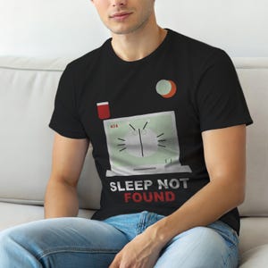 May include: Black t-shirt featuring a computer screen graphic with a clock design and the words "SLEEP NOT FOUND." The design includes a red rectangle and a half-circle in orange and white.