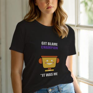 May include: Black t-shirt featuring the text "GIT BLAME CHAMPION" in purple and a cartoon trophy graphic. The trophy is yellow with orange handles and the text "IT WAS ME" below it.