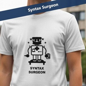 Op de afbeelding: Wit t-shirt met een zwarte afbeelding van een robot die een medisch symbool en een kleine container vasthoudt. De tekst "Syntax Surgeon" staat onder de robot en op een blauwe banner boven het shirt.