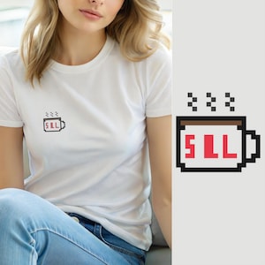 Peut inclure: Un t-shirt blanc à manches courtes avec un petit motif en pixel art sur la poitrine. Le motif représente une tasse blanche avec un bord marron, des contours noirs et trois petites marques de vapeur noires au-dessus. Les lettres SLL sont rouges.