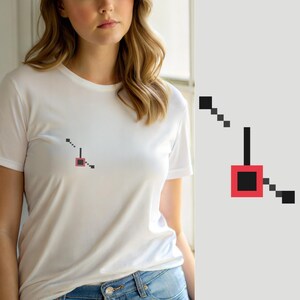 Puede incluir: Una camiseta blanca de manga corta con un pequeño gráfico de arte de píxeles en el pecho. El diseño consiste en un cuadrado rojo con un centro negro, conectado a una serie de pequeños cuadrados negros dispuestos en línea diagonal y una barra vertical.