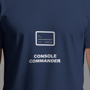 Op de afbeelding: Marineblauw t-shirt met de witte tekst "CONSOLE COMMANDER". Boven de tekst staat een witte rechthoek met de tekst "run --deploy" en een opdrachtpromptsymbool.