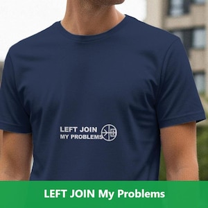 May include: Navy blue t-shirt with the text "LEFT JOIN MY PROBLEMS" in white, along with a graphic. The shirt is short-sleeved and made of a soft material. The image is taken outdoors, with a blurred background of buildings.