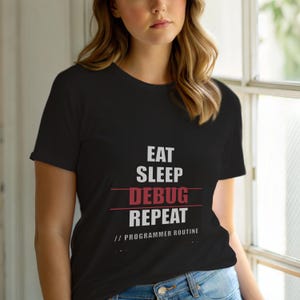 Może przedstawiać: Czarny t-shirt z napisem "EAT SLEEP DEBUG REPEAT // PROGRAMMER ROUTINE" w kolorze białym i czerwonym. Koszulka ma okrągły dekolt.