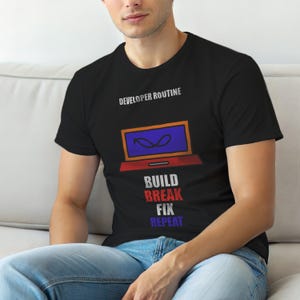 Op de afbeelding: Zwart T-shirt met de tekst "DEVELOPER ROUTINE" boven een laptopafbeelding. De laptop heeft een blauw scherm en een rode basis. Daaronder staan de woorden "BUILD BREAK FIX REPEAT" gestapeld.