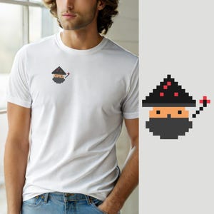 Peut inclure: Un t-shirt blanc à manches courtes avec un petit graphique en pixel art sur la poitrine gauche. Le motif représente un personnage portant un chapeau pointu noir avec des accents rouges, un visage beige, une barbe gris foncé et une baguette rouge.