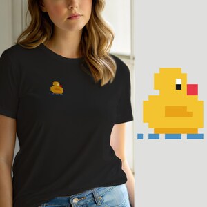 May include: A black short-sleeved t-shirt featuring a small pixel art graphic of a yellow rubber duck on the left chest. The duck design is rendered in a blocky, digital style with a red beak, a white eye, and blue water ripples underneath.