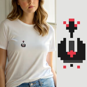 May include: A white short-sleeved t-shirt featuring a small, centered pixel art graphic. The design consists of a black and dark gray abstract shape with red pixel accents, resembling a stylized character or icon, positioned on the chest area.