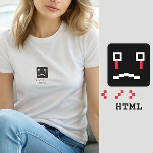 May include: A white short-sleeved t-shirt featuring a small graphic on the chest. The graphic displays a black square with a pixelated sad face, red pixelated tears, red pixelated brackets, and the black text HTML printed underneath the icon.