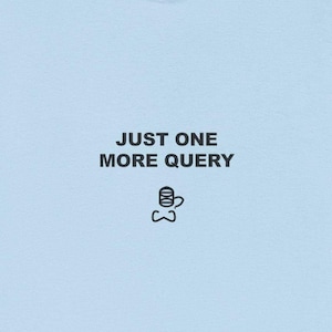 May include: A pale blue t-shirt featuring the black text "JUST ONE MORE QUERY" and a small graphic of a coffee cup and bow tie. The shirt is made of a soft material.