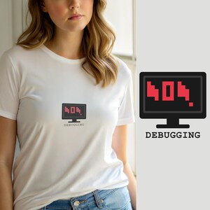 Op de afbeelding: Een wit t-shirt met korte mouwen en een afbeelding van een zwarte computermonitor met de rode, gepixelde tekst 404. Onder het monitorpictogram staat het woord DEBUGGING in een zwart lettertype in typemachinestijl op de borst.
