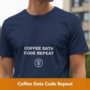 May include: Navy blue t-shirt with the text "COFFEE DATA CODE REPEAT" in white, along with a small graphic. The shirt is a crew neck style and appears to be made of a soft material. The image is taken outdoors.