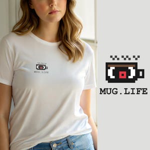 Op de afbeelding: Een wit T-shirt met korte mouwen en een kleine pixel-art afbeelding op de linkerborst. De afbeelding toont een zwarte koffiemok met een bruine bovenkant, een rood vierkant in het midden en de tekst MUG.LIFE in een zwart pixellettertype.