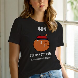 May include: Black t-shirt with a humorous graphic. The design features a sleeping orange character wearing a red cap, with the text "404 Sleep Not Found Debugging Since Midnight."